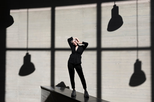 Stylish businesswoman wearing suit standing on retaining wall with sunlight and shadow in background