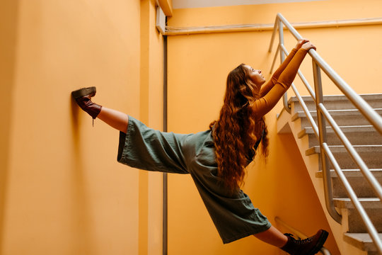 Young woman wearing jumpsuit standing on railing in front of orange wall