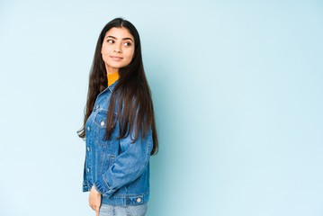 Young indian woman isolated on blue background looks aside smiling, cheerful and pleasant.