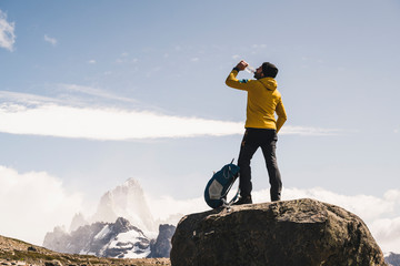 Male hiker drinking water while standing on rock against sky, Patagonia, Argentina