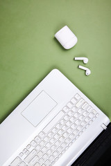 View from above on a open white laptop, wireless headphones and a close white case. Isolated green background. Top view.