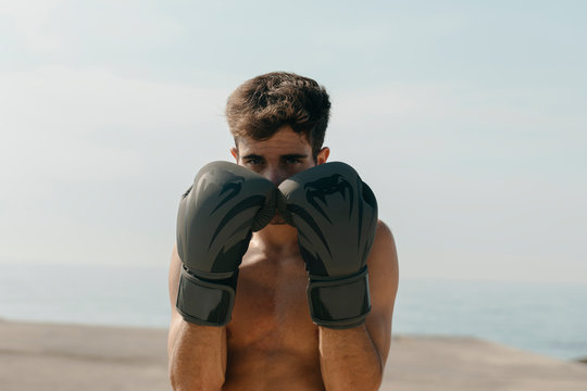 Close-up of shirtless boxer wearing gloves while standing at harbor against clear sky