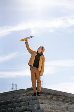 Boy holding rocket toy while standing on steps against sky