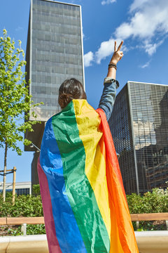 Woman gesturing peace sign while carrying rainbow flag in city