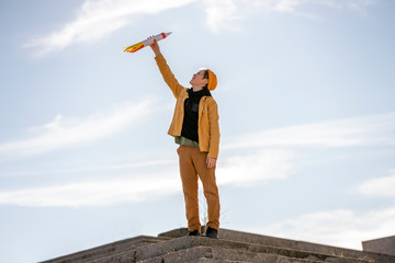 Boy holding rocket toy while standing on steps against sky