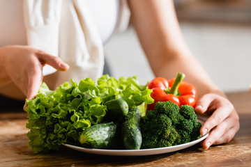 selective focus of woman touching plate with vegetables