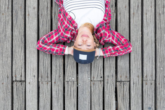Mid adult woman wearing cap with hands behind head lying on bridge