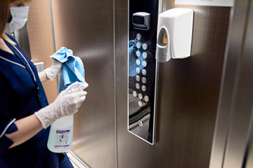 Chambermaid wearing mask cleaning elevator buttons in hotel