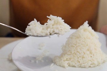In selective focus a man hand holding a spoon of Jasmine rice with blurred a white dish on a dinning table 