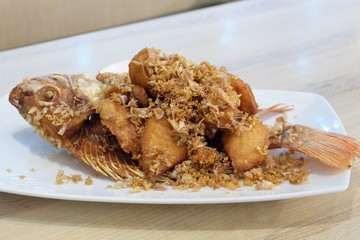 Fried crispy garlic red Tilapia fish on a white plate on a dinning table 