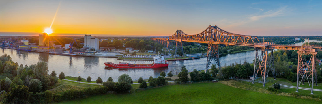 Panoramic aerial view of famous railway Rendsburg High Bridge with cargo ship and the camping caravan area by evening