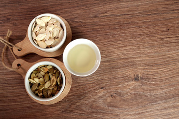 Pumpkin seed oil in a glass dish and peeled pumpkin seeds. pumpkin seeds are not peeled. on a brown rustic traditional wooden table.with place for text on the right. banner