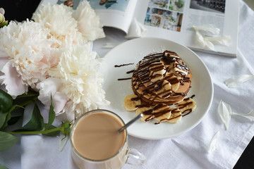 pancakes poured with chocolate with banana and a cup of coffee with milk