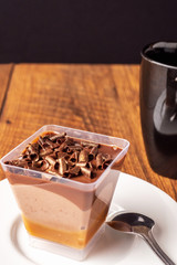 Chocolate dessert with chunks of chocolate on a white plate with tea spoon and black cup with tea on a wooden table surface. Concept desert, tea time.