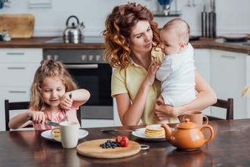 selective focus of mother holding infant son near daughter eating pancakes