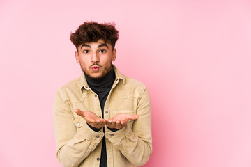 Young arabian man posing in a background isolated folding lips and holding palms to send air kiss.