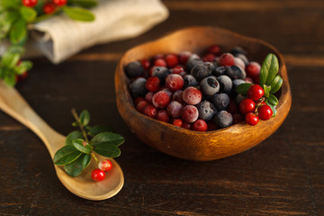 frozen cranberries and blueberries in a wooden bowl, decorated with a sprig of fresh cranberries