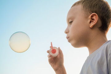 Boy blowing soap bubble on the blue sky background