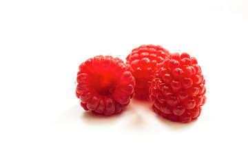 Red ripe fresh raspberries on white surface close-up. Three berry of raspberry. Limited depth of field.