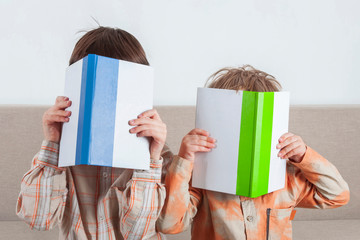 Two boys read books. They cover their faces with a book. (concept of friendship, intelligence)
