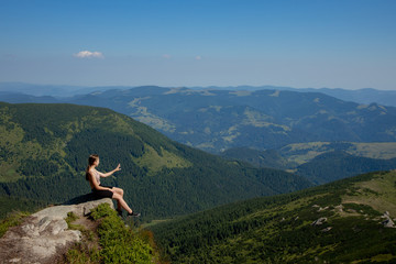 Naklejka na ściany i meble A girl sits on the edge of the cliff and looking at the sun valley and mountains