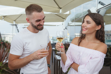 Gorgeous woman laughing, enjoying drinking wine with her boyfriend at rooftop bar