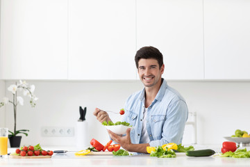 Handsome man eating salad with fresh vegetables in the kitchen.