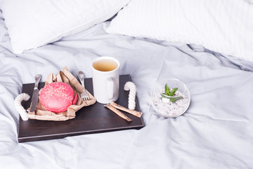 Breakfast in bed on wooden tray pink burgerand and coffe. Window light, copy space