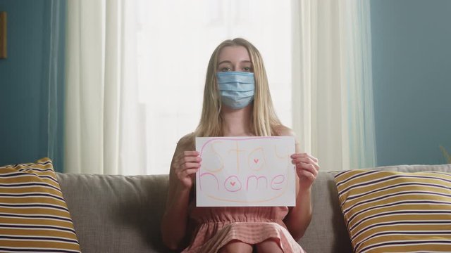 A young girl with a medical bandage in her hands on her face sits on a beige sofa and holds a sheet of white paper