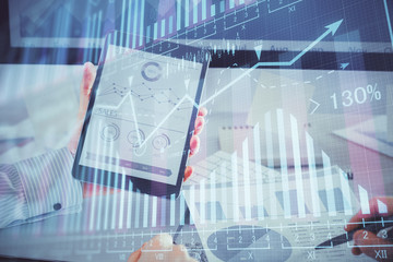 Double exposure of man's hands holding and using a digital device and forex graph drawing. Financial market concept.