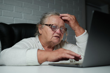 Senior Woman Using Laptop In light room. Elderly woman's hands on a computer keyboard in the dark, light from the screen. The older generation is searching for information and working 