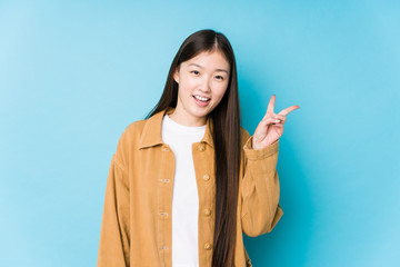 Young chinese woman posing in a blue background isolated joyful and carefree showing a peace symbol...