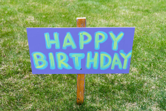 Happy Birthday Party Home Made Sign Staked In A Grass Lawn. Signpost Message In Writing, Banner In A Park