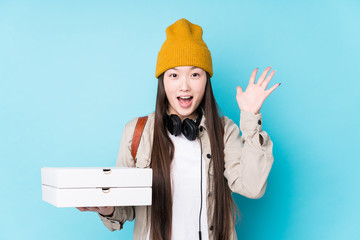 Young chinese woman holding pizzas isolated receiving a pleasant surprise, excited and raising hands.