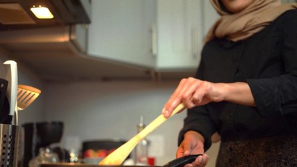 Photo of a veiled woman who is cooking in a modern kitchen