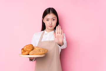 Young chinese baker woman isolated standing with outstretched hand showing stop sign, preventing you.