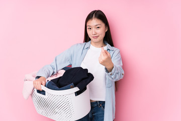 Young chinese woman picking up dirty clothes isolated pointing with finger at you as if inviting...