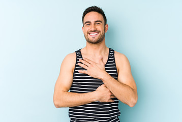 Young caucasian man isolated on blue background laughs happily and has fun keeping hands on stomach.