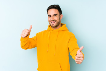Young caucasian man isolated on blue background raising both thumbs up, smiling and confident.