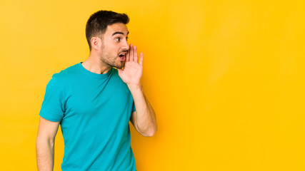 Young caucasian man isolated on yellow bakground is saying a secret hot braking news and looking...