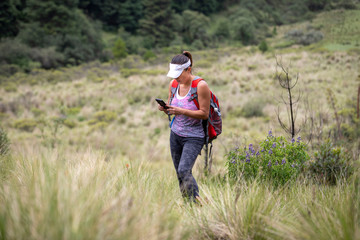 Naklejka na ściany i meble mexican young adult woman standing in a valley on a summer day with cell phone in her hands