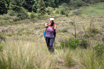 mexican young adult woman standing in a valley on a summer day with cell phone in her hands taking an image