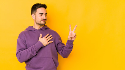 Young caucasian man isolated on yellow bakground taking an oath, putting hand on chest.