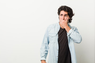 Young handsome man against a white background thoughtful looking to a copy space covering mouth with hand.