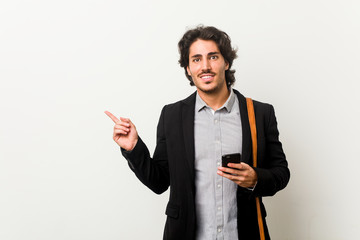 Young business man holding a phone smiling and pointing aside, showing something at blank space.