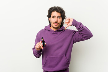 Young man holding a vaporizer showing a dislike gesture, thumbs down. Disagreement concept.