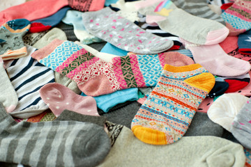 Lots of socks on the table. Socks of different sizes and colors for the cold season. Knitted clothes for autumn. A pile of socks create the background.