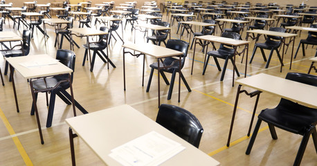 A view looking down on a large secondary high school exam hall set up with organized desks table and papers ready for students to sit the examination.
