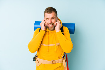 Senior hiker man isolated on blue background covering ears with hands.