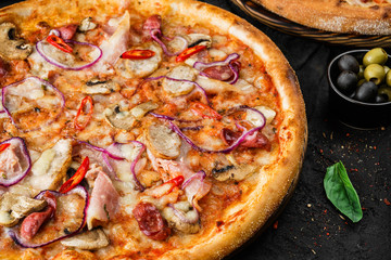 Pizza Pepperoni with prosciutto, sausage, ham, cheese parmesan, tomatoes and onion rings, mushrooms on stone black background. Fast food lunch for picnic company, close up, selective focus
